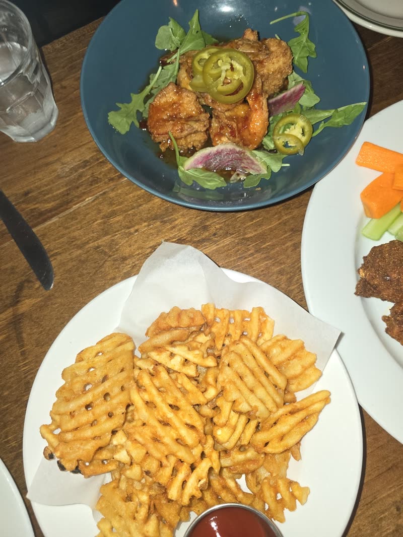 A table spread of fried chicken on salad with waffle fries and dipping sauce