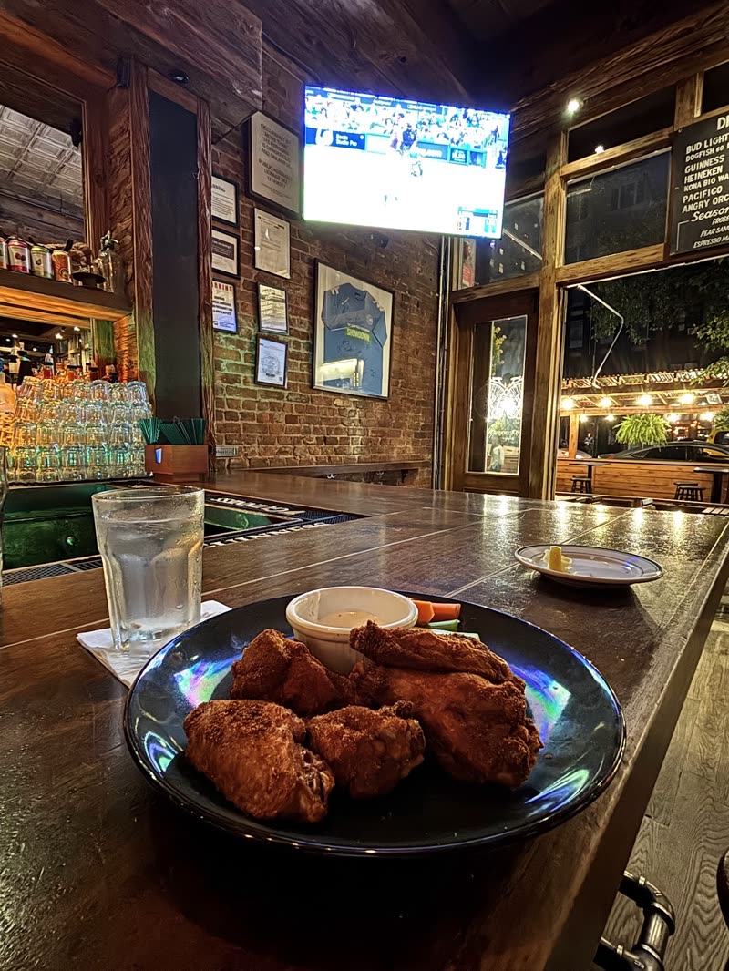A bowl of fried chicken wings and a glass of water on the polished bar, room and TV behind