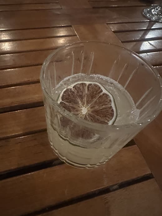 A tall clear cocktail with a lime wheel on a slatted wooden table